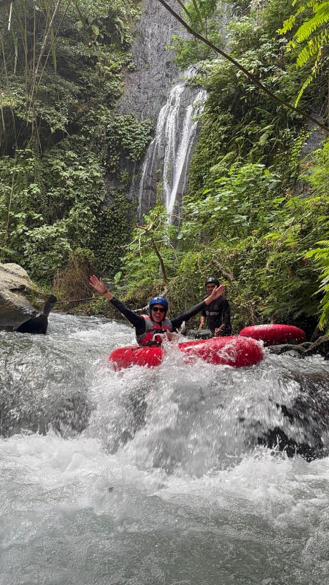 Des participants exultent sous une haute cascade de jungle sur le parcours de tubing