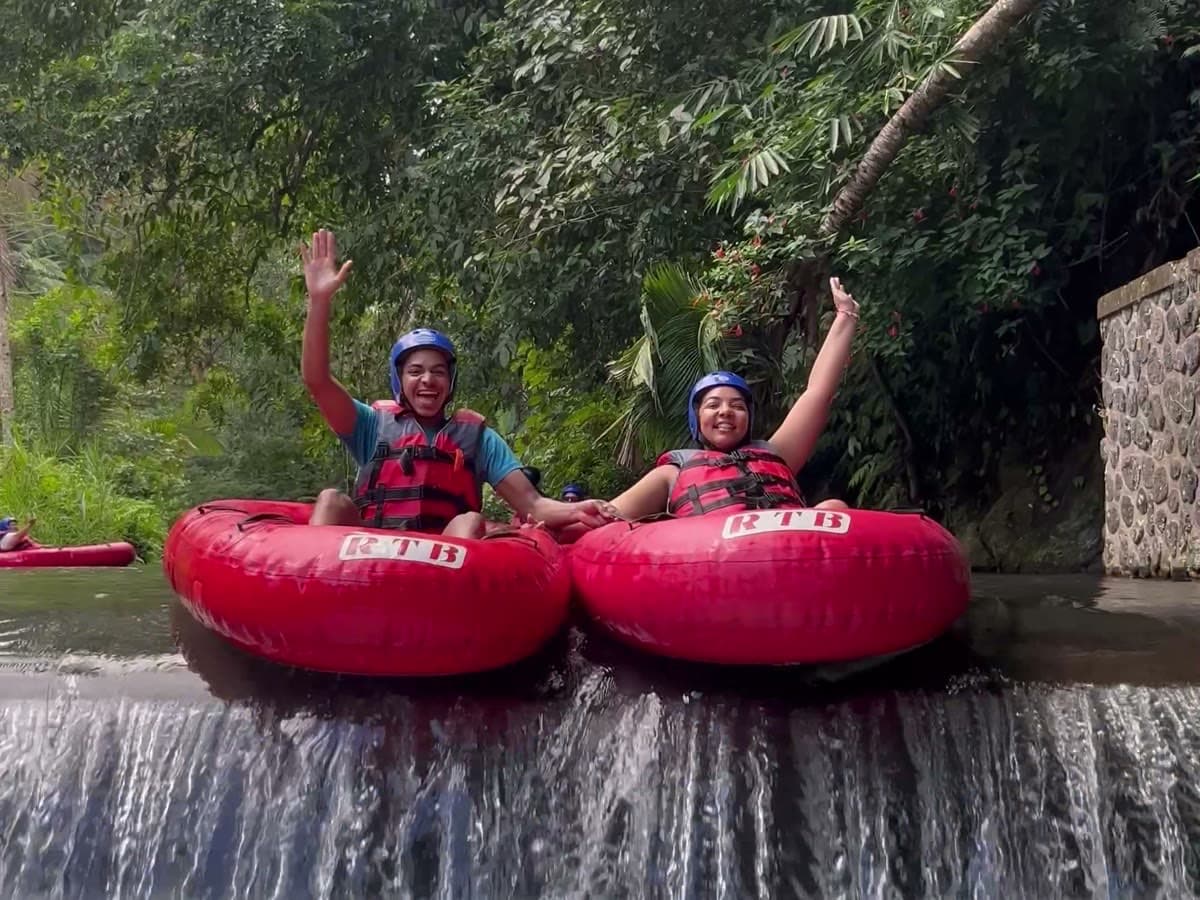 Two riders wave as they drop over a river weir while tubing in Ubud