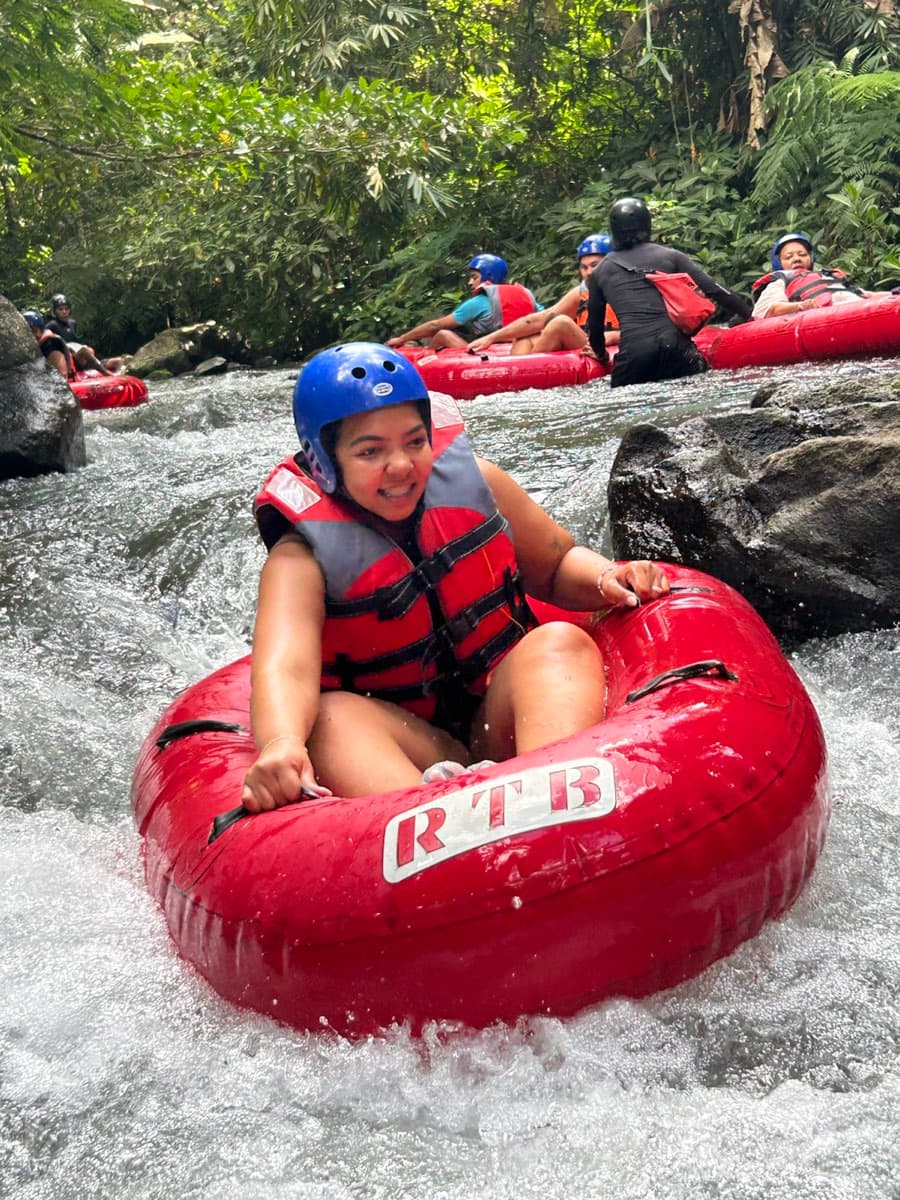 A smiling rider floats down the jungle rapids in a red tube