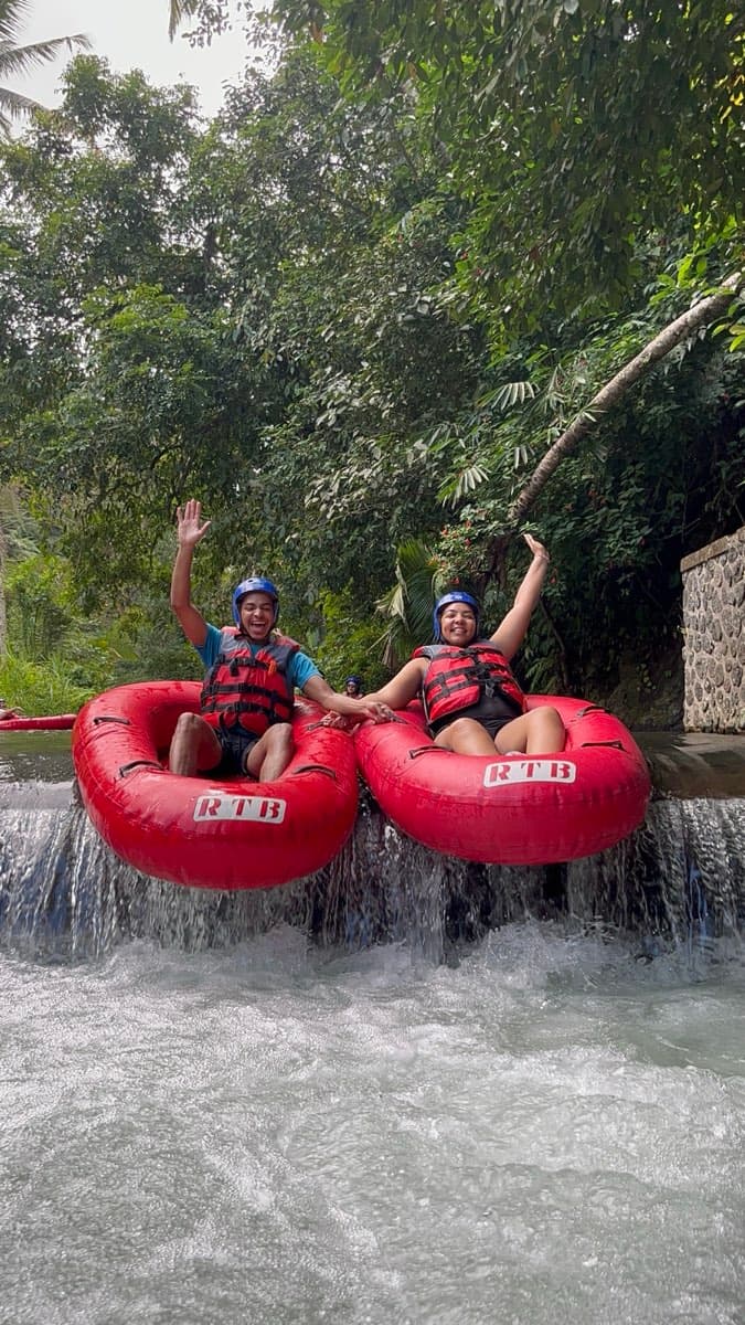 Two riders drop side by side over a river weir, waving