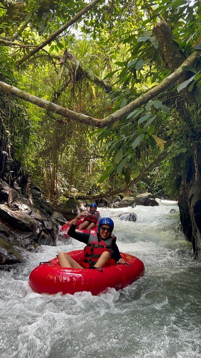 Two tubers drift through a narrow vine-draped jungle gorge