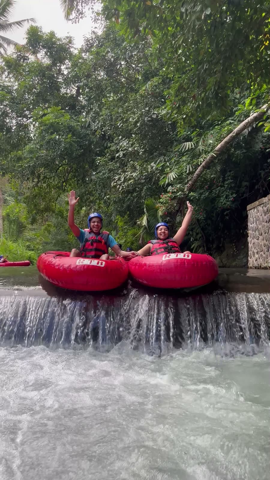 Two riders wave as they drop over a river weir while tubing in Ubud